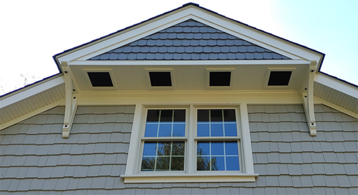 Close-up of a house gable with two windows and shingle siding under a blue sky.