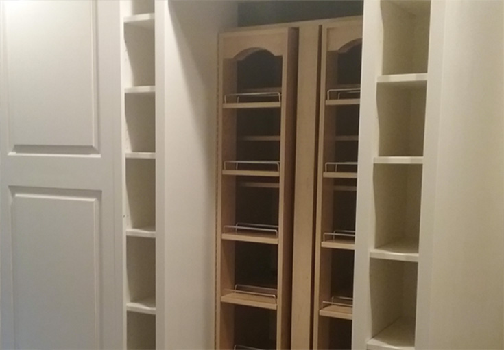 A walk-in closet construction with built-in wooden shelves and cabinet doors.