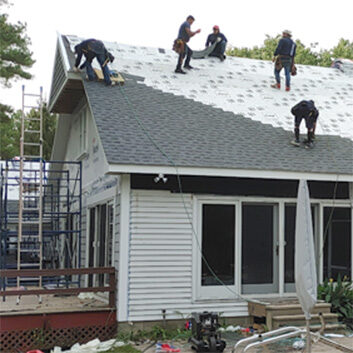 Workers installing a roof on a residential house with scaffolding on the side.