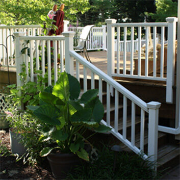 A close-up of a deck stairway with white railings and large potted plants nearby.