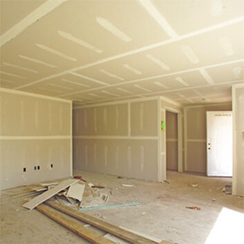 An unfinished room under construction with exposed drywall and taping, debris on the floor, and a door in the background.